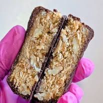 A pink-gloved hand holding a cookie bar cut in half