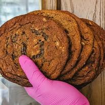 A pink-gloved hand holding a stack of big cookies