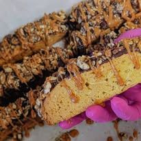 A pink-gloved hand holding a drizzled cookie bar