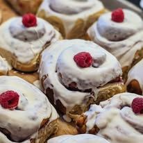 Glazed cinnamon rolls each topped with a fresh raspberry